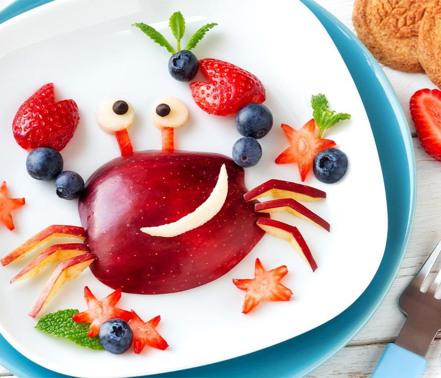 Fun Food for kids. Cute smiling crab made of fresh fruits - apple, strawberry, blueberries and fresh mint - for a healthy breakfast with milk and biscuits